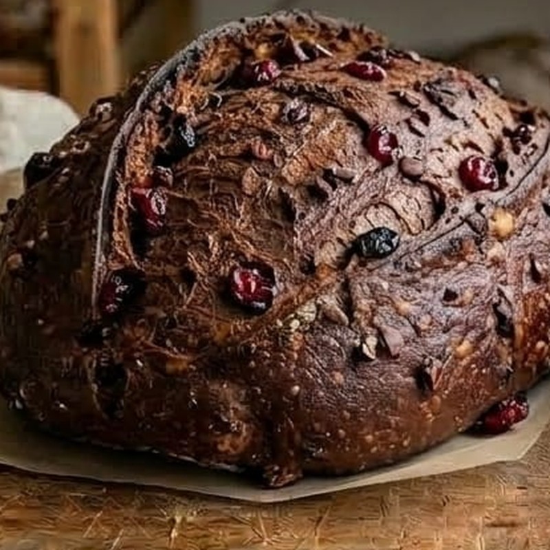 Pão sourdough escuro de cacau com cranberries no miolo, fatiado sobre tábua rústica